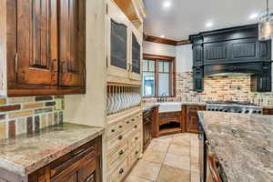 Kitchen with backsplash, crown molding, light stone counters, glass fronted cabinets, and stainless steel gas cooktop