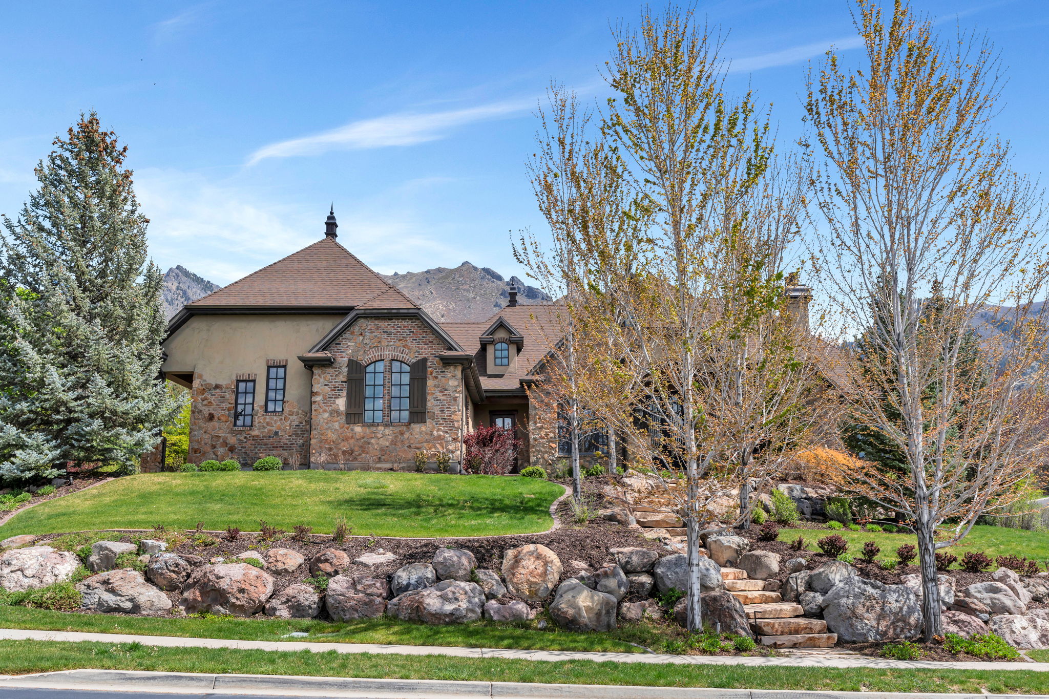 View of front of home with a mountain view, stone siding, a front lawn, and stucco siding