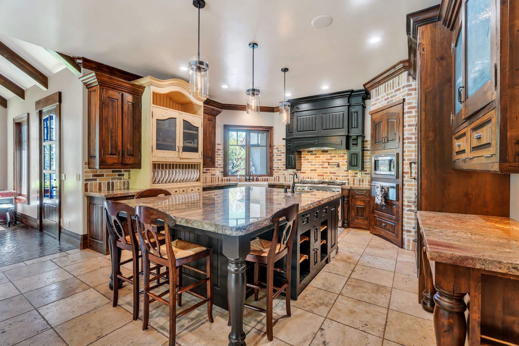 Two tone kitchen with glass insert cabinets, a kitchen breakfast bar, backsplash, a kitchen island with sink, and light stone counters