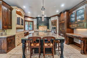 Kitchen with glass fronted cabinets, a breakfast bar, an island with sink, crown molding, and backsplash