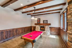 Playroom with a wainscoted wall, wooden walls, billiards table, carpet, and a stone fireplace