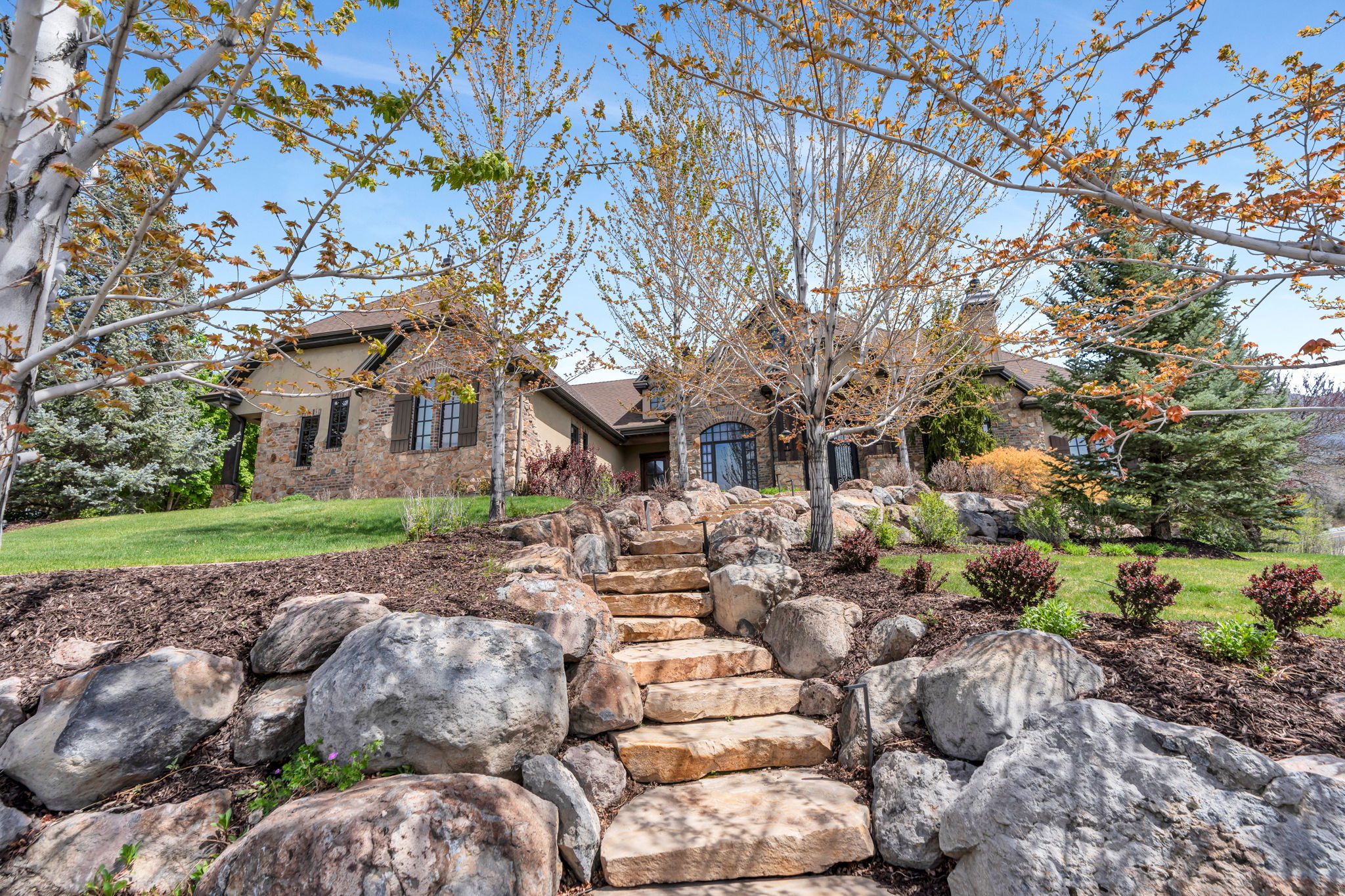 View of front of home featuring a front yard, a chimney, stone siding, and stucco siding