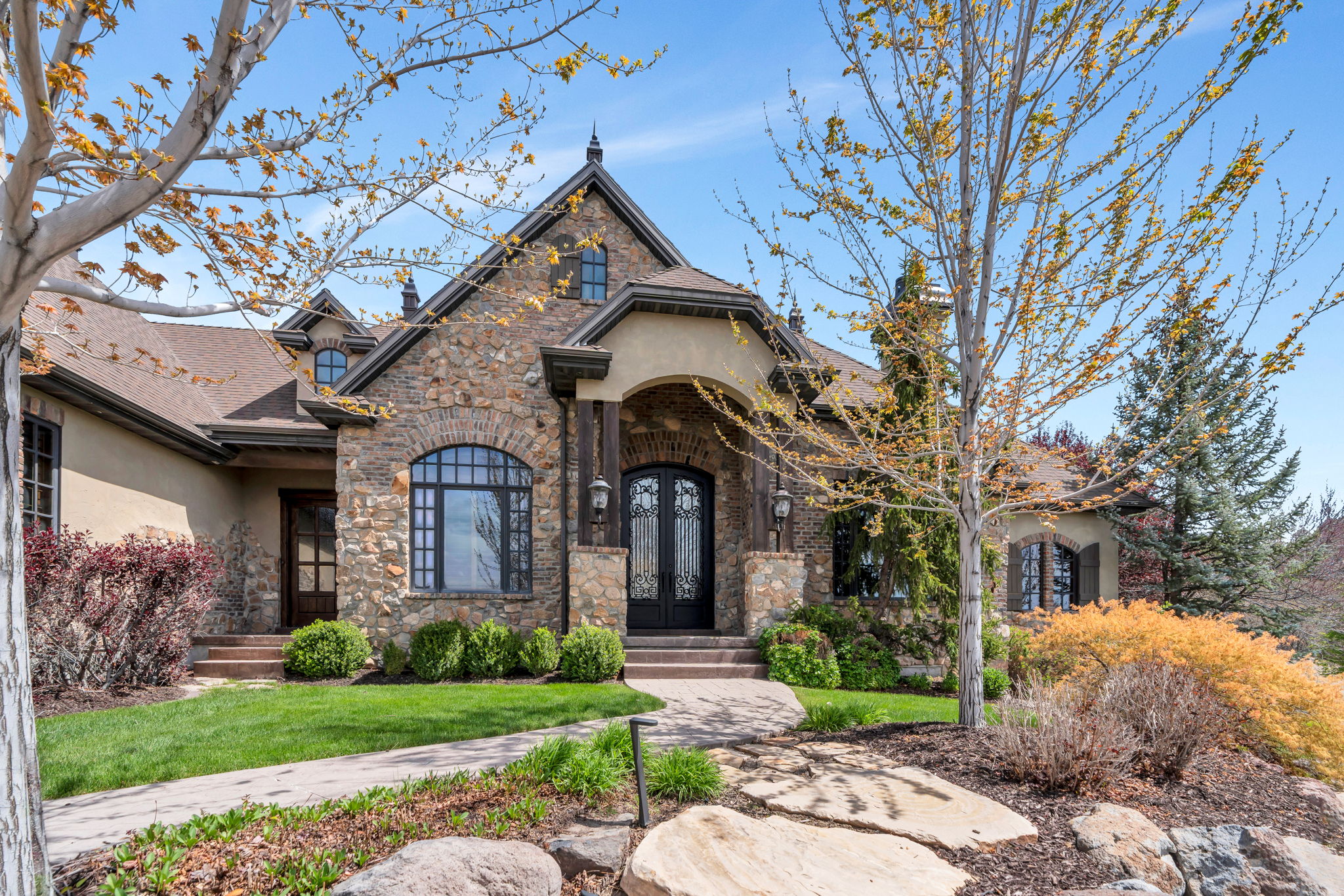 French country inspired facade featuring stucco siding, stone siding, a front lawn, and a shingled roof