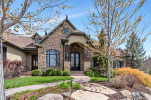 French country inspired facade featuring stucco siding, stone siding, a front lawn, and a shingled roof