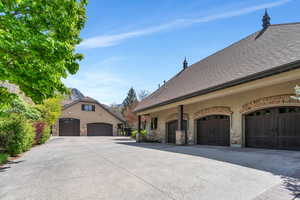View of home's exterior featuring stone siding, a shingled roof, a garage, stucco siding, and driveway