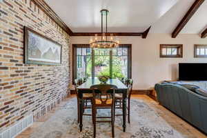 Dining room with brick wall, hanging lights, beamed ceiling, and stone tile flooring