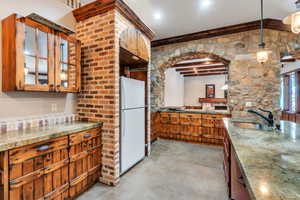 Kitchen with concrete floors, freestanding refrigerator, hanging light fixtures, wood finish cabinets, and glass insert cabinets
