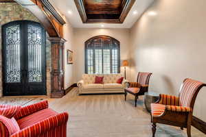 Living area featuring french doors, arched walkways, a raised ceiling, light carpet, and recessed lighting