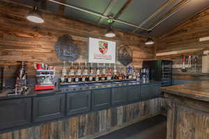 Indoor dry bar with wood walls, hanging light fixtures, black refrigerator, butcher block counters, and lofted ceiling