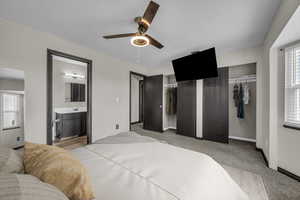 Bedroom with multiple windows, two closets, light colored carpet, and ceiling fan