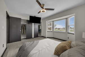 Bedroom with two closets, light colored carpet, ceiling fan, and a textured ceiling