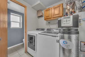 Laundry room featuring light tile patterned floors, washer and dryer, a textured ceiling, cabinet space, and water heater