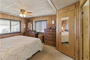 Main ensuite bedroom with light colored carpet, ceiling fan,  wooden walls, and walk in closet.