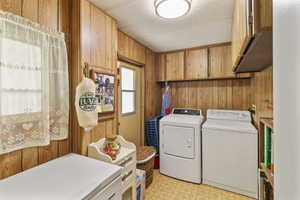Laundry room with light floors, wood walls, cabinet space, and washer and dryer hook ups. This door exits to the west carport for easy access to bring in groceries.