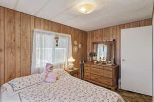 Bedroom with dark colored carpet and wooden walls. Large closet with sliding doors at the foot of the bed, not pictured.