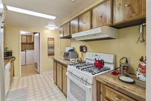 Kitchen with light flooring, white appliances, wood finish cabinets, pantry, and laundry room adjacent with washing machine and clothes dryer.