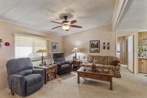 Living area featuring light carpet, vaulted ceiling with beams, and ceiling fan.