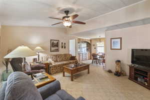 Living area with a ceiling fan, light carpet, vaulted ceilings.