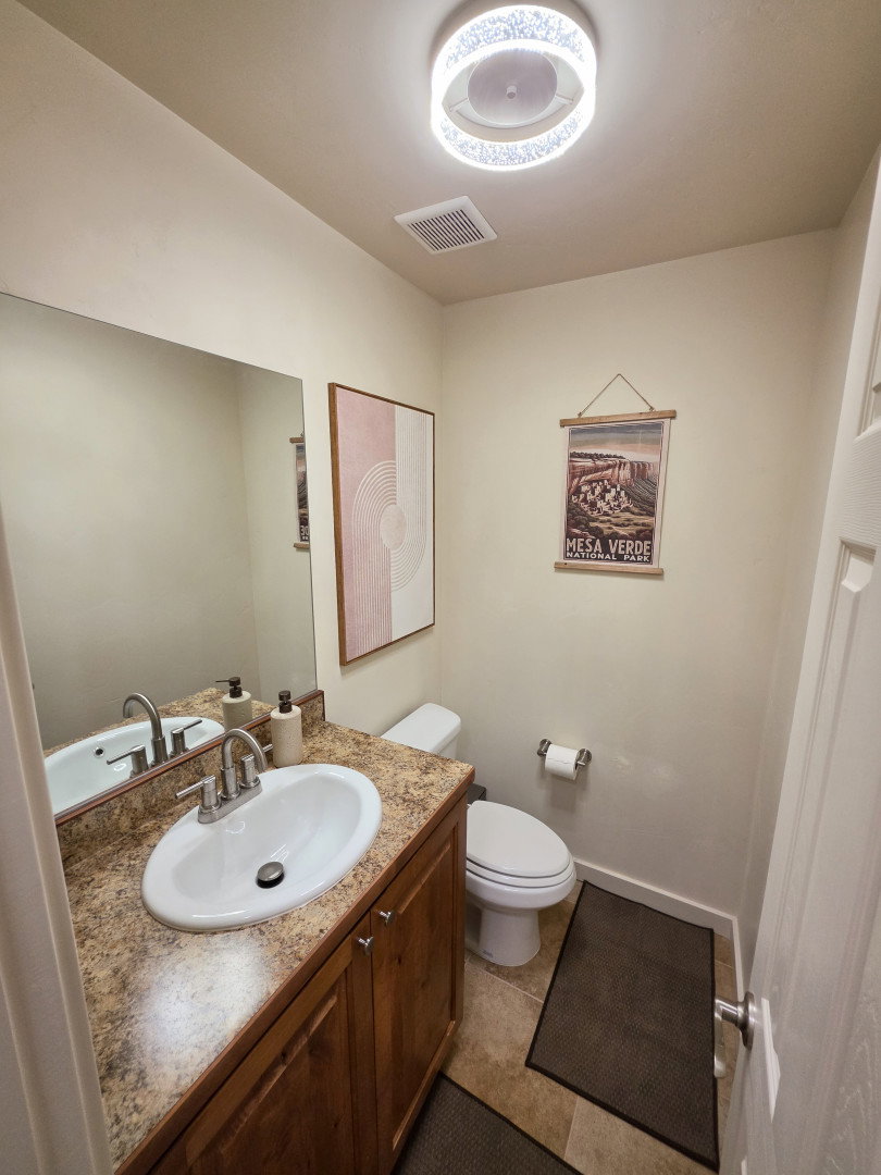 Powder room featuring a wood-finish vanity with an oval sink, speckled countertop, and a large wall-mounted mirror