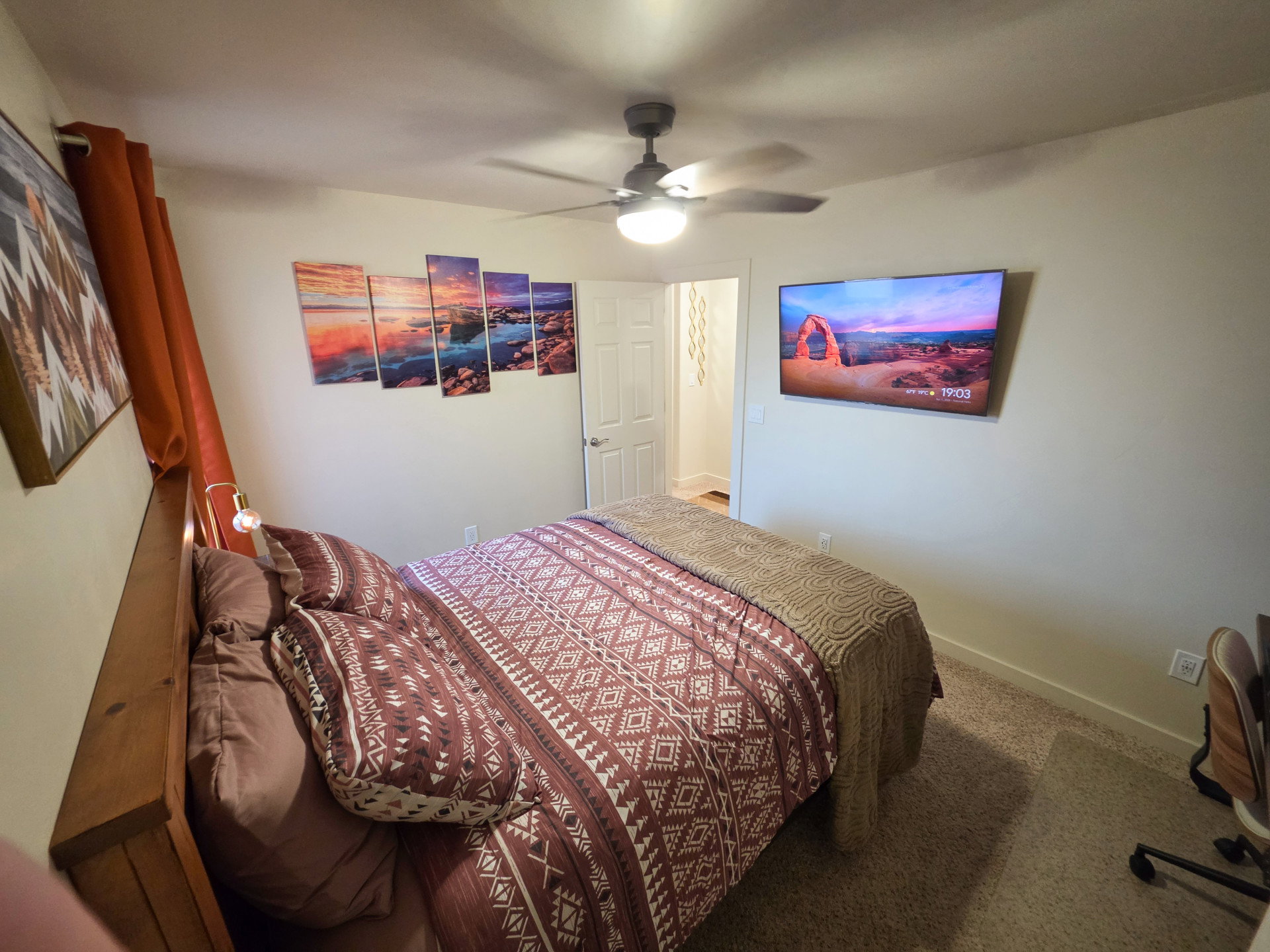 Bedroom featuring a ceiling fan with integrated lighting, wall-mounted television, and wood-finish headboard