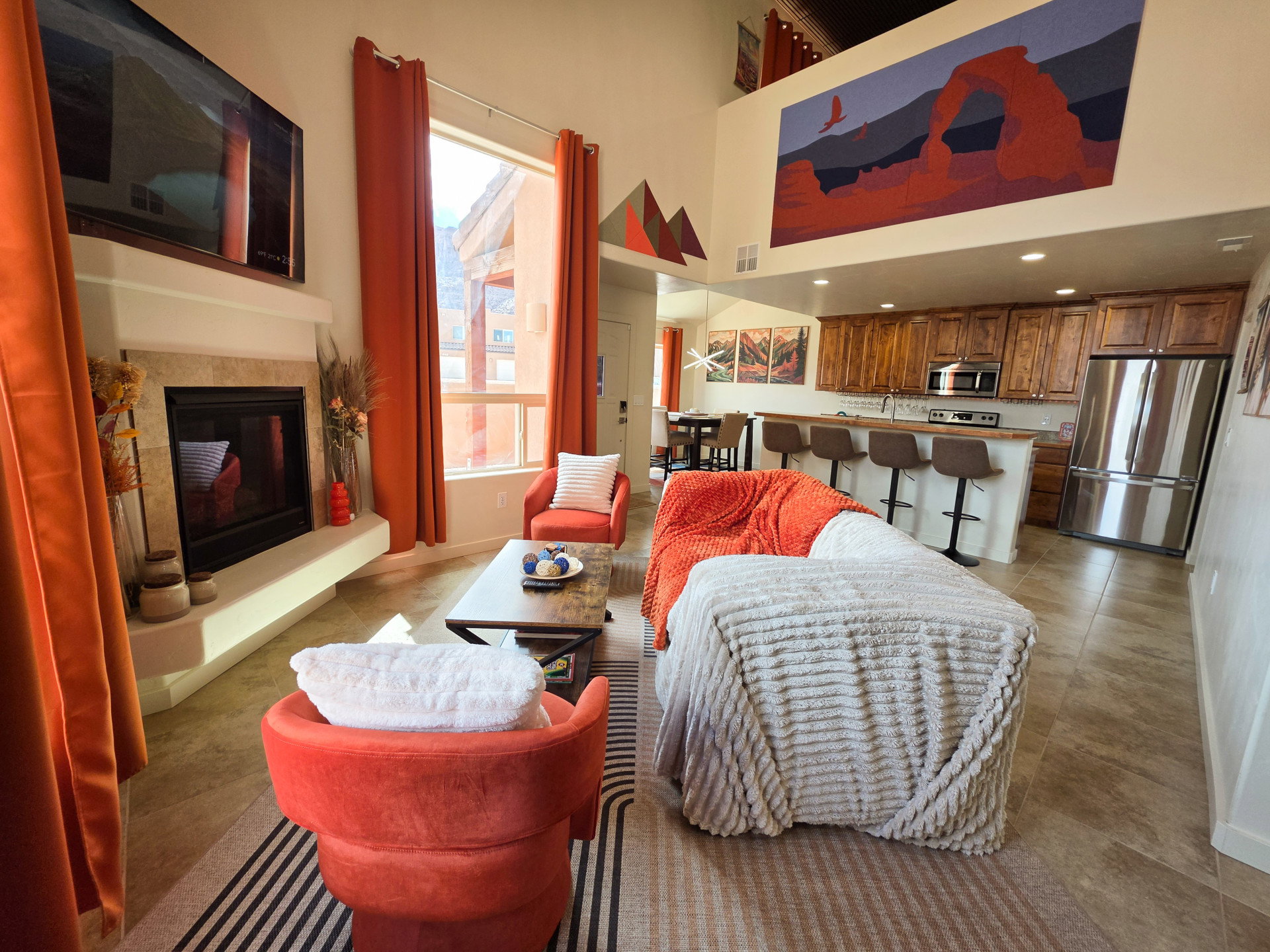 Vaulted living area featuring a fireplace with a stone surround, tile flooring, and large windows