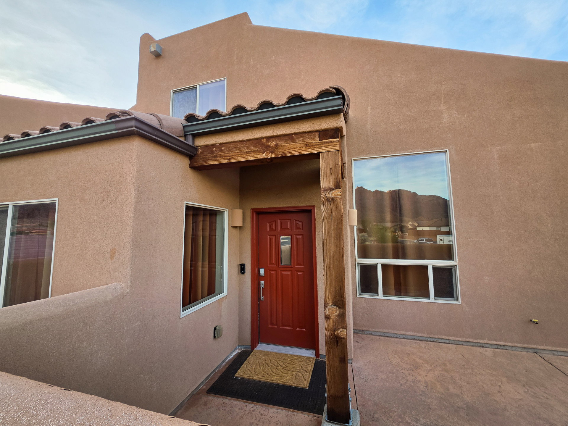 Stucco exterior featuring a prominent red entry door, decorative tile roof, and rough-hewn wood porch beams