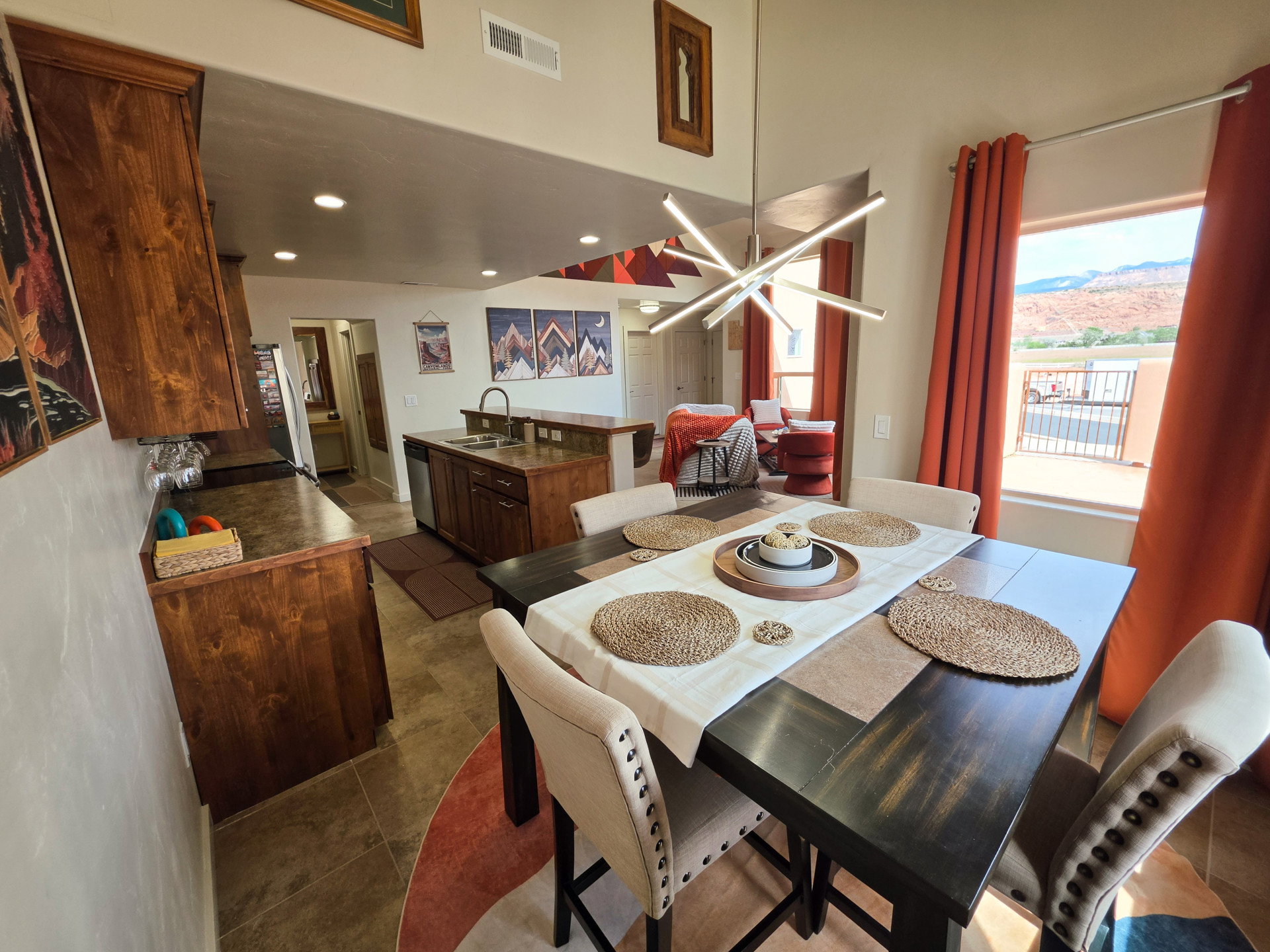 Open-concept dining area featuring a modern linear chandelier, wood-finish flooring, and a window with mountain scenery