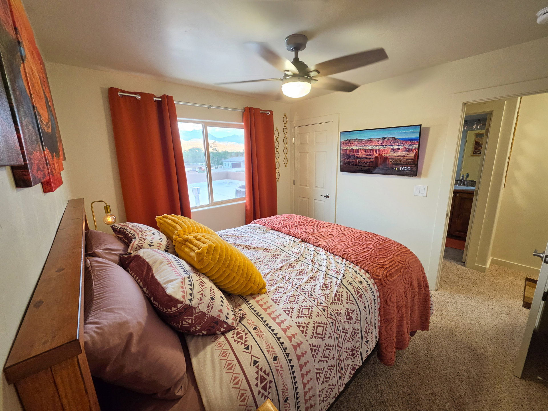 Bedroom featuring a ceiling fan with integrated lighting, wall-mounted television, and a window with roller shades