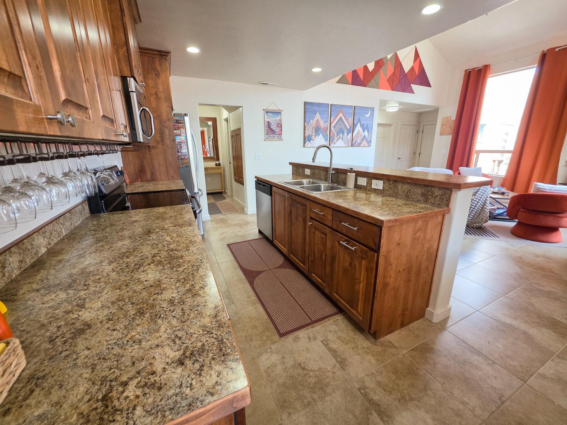 Kitchen featuring wood cabinetry with brushed nickel hardware, laminate countertops, a stainless steel double basin sink with a high-arc faucet, and tiled flooring