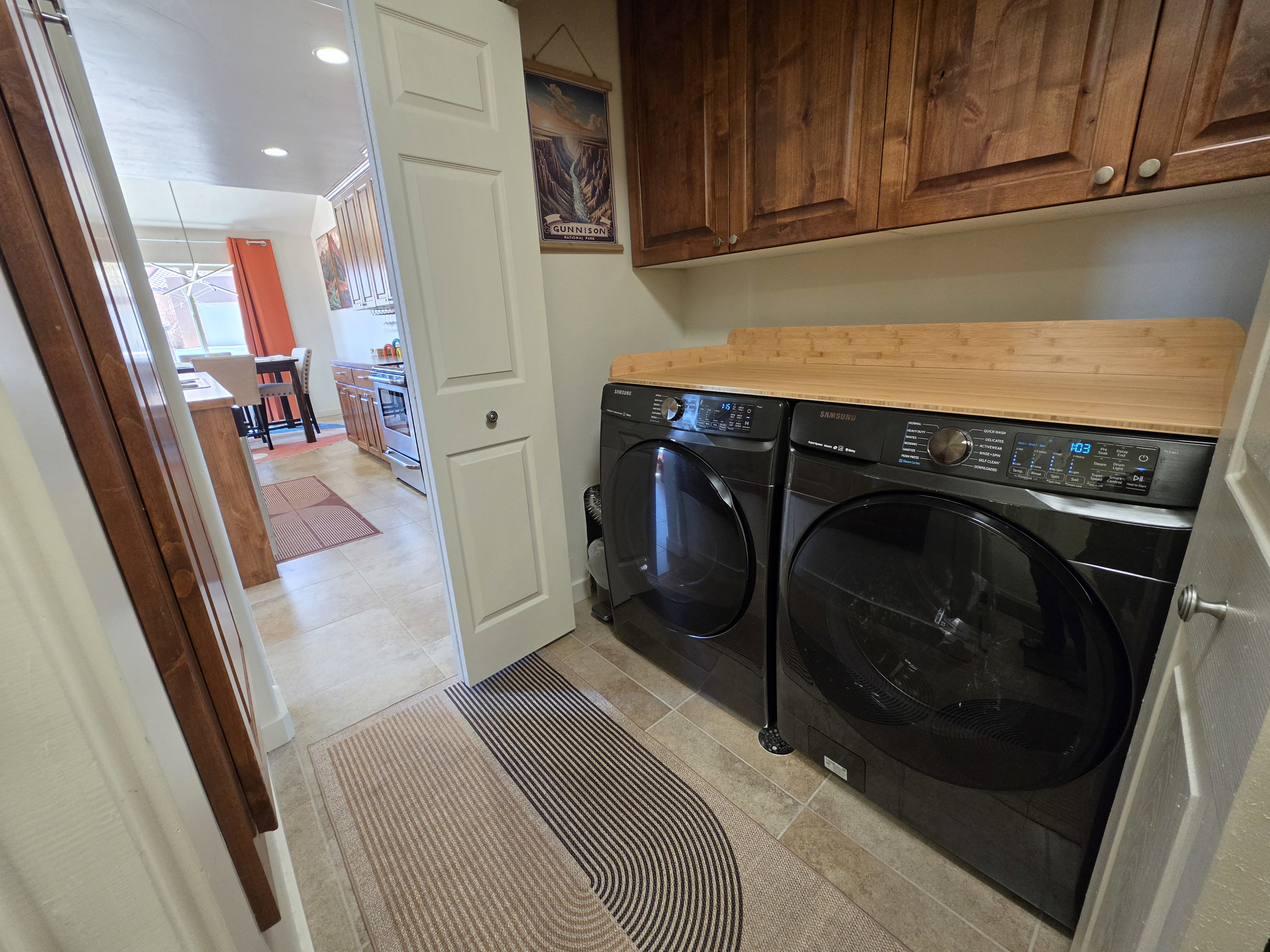 Dedicated laundry area featuring dark cabinetry, a natural wood-finish countertop, and durable tile flooring