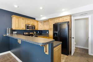 Kitchen featuring a breakfast bar, dark countertops, a peninsula, stainless steel appliances, and light wood finish cabinetry