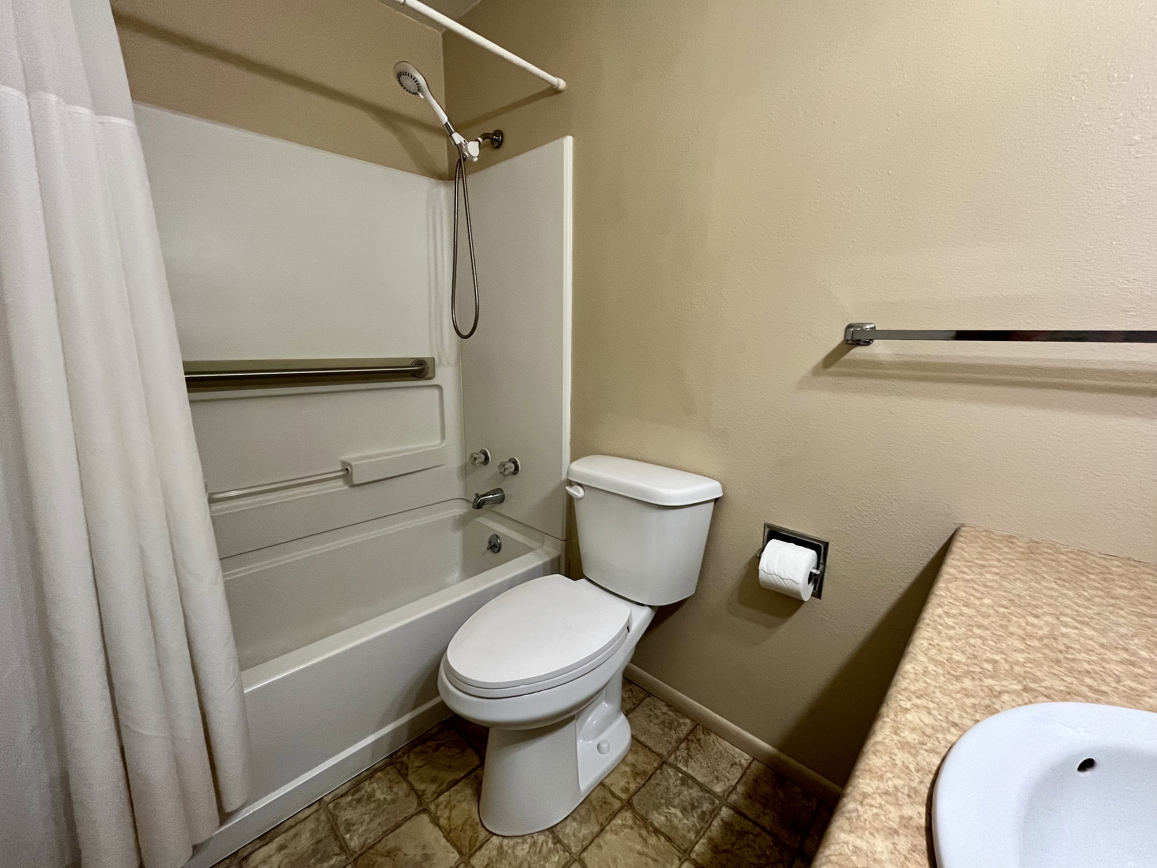 Bathroom featuring shower / bathtub combination with curtain, vanity, and stone finish flooring