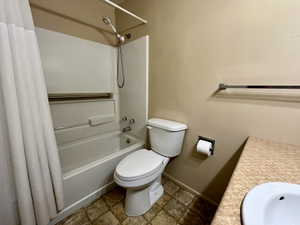 Bathroom featuring shower / bathtub combination with curtain, vanity, and stone finish flooring