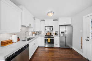 Kitchen featuring stainless steel appliances, white cabinets, decorative backsplash, dark wood-style flooring, and light stone counters
