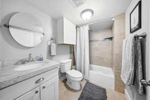 Full bathroom featuring vanity, shower / bathtub combination with curtain, light tile patterned floors, and a textured ceiling