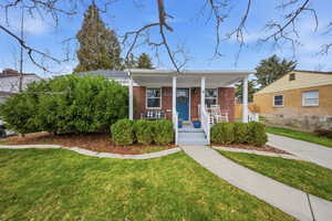 Bungalow-style home with covered porch, a front yard, and brick siding