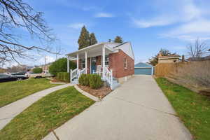 Bungalow-style home with brick siding, a detached garage, an outdoor structure, covered porch, and a front yard