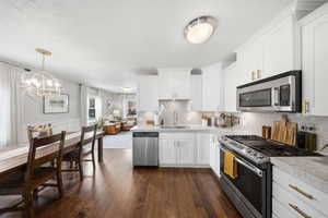 Kitchen featuring stainless steel appliances, light countertops, white cabinetry, dark wood finished floors, and hanging lights
