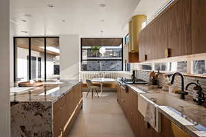 Kitchen with modern cabinets, light stone countertops, wood finish cabinetry, hanging light fixtures, and stainless steel gas stovetop