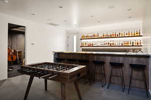 Recreation room with bar with sink, dark tile patterned flooring, and recessed lighting
