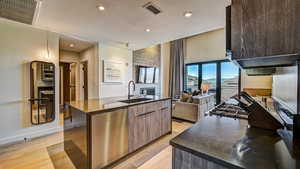 Kitchen with modern cabinets, stainless steel dishwasher, a center island with sink, light wood-type flooring, and open floor plan