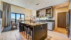 Kitchen featuring open shelves, dark stone countertops, a kitchen bar, light wood finished floors, and recessed lighting