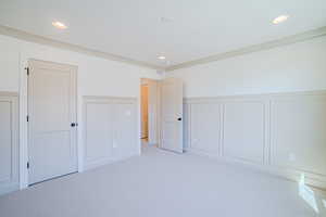 Unfurnished bedroom featuring a decorative wall, wainscoting, and light colored carpet