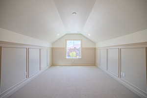Bonus room featuring a decorative wall, light colored carpet, a textured ceiling, and wainscoting