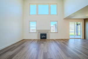 Unfurnished living room with a tile fireplace, a high ceiling, dark wood-type flooring, and plenty of natural light