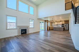 Unfurnished living room featuring suspended lighting, a fireplace, dark wood-type flooring, a high ceiling, and healthy amount of natural light