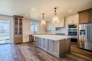 Kitchen with dual tone cabinetry, stainless steel appliances, decorative backsplash, a center island, and dark wood-style flooring