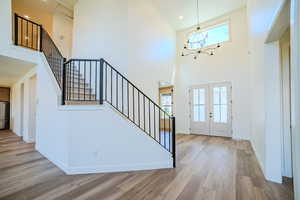 Foyer entrance with plenty of natural light, light wood-style flooring, a high ceiling, suspended lighting, and french doors
