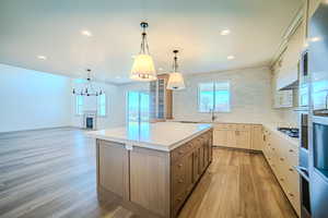 Dual tone kitchen featuring two tone color scheme, backsplash, a kitchen island, a glass covered fireplace, and light wood finished floors