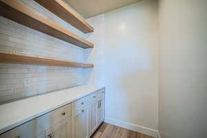 Bar area with open shelves, decorative backsplash, light wood-style floors, and light stone countertops